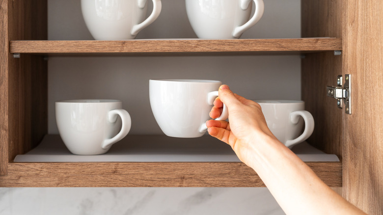 Person removing white mug from cabinet shelf