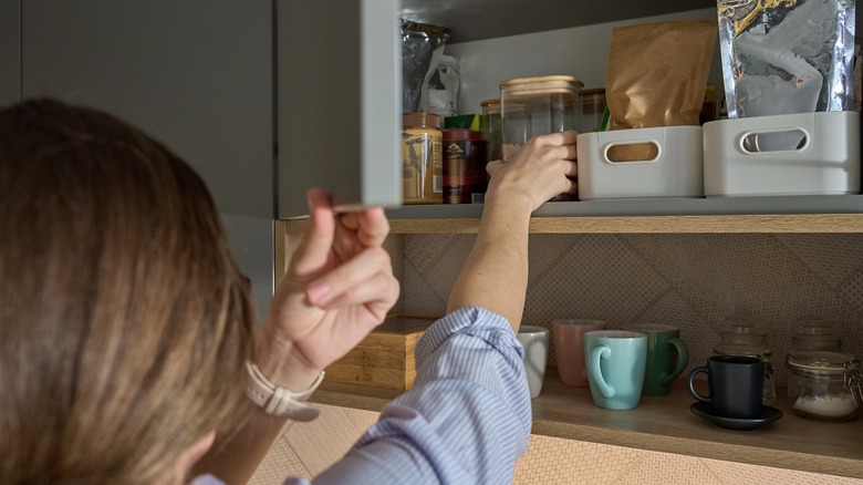 Person reaching into kitchen cabinet with plastic baskets and jars.