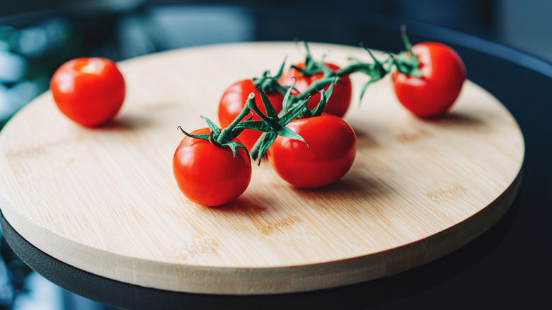 Cherry tomatoes with stems on a circular wooden cutting board.