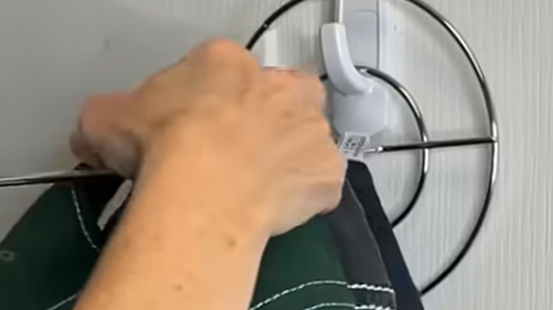 An influencer hangs ball caps from a long, horizontal hanger in a closet created by turning a metal paper towel holder sideways and hanging the base from a self-adhesive hook.