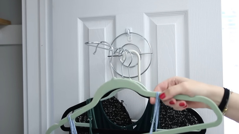 An influencer hangs clothes on the back of a closet door on an extended hanger she created using a metal paper towel holder hung horizontally on a self-adhesive hook.