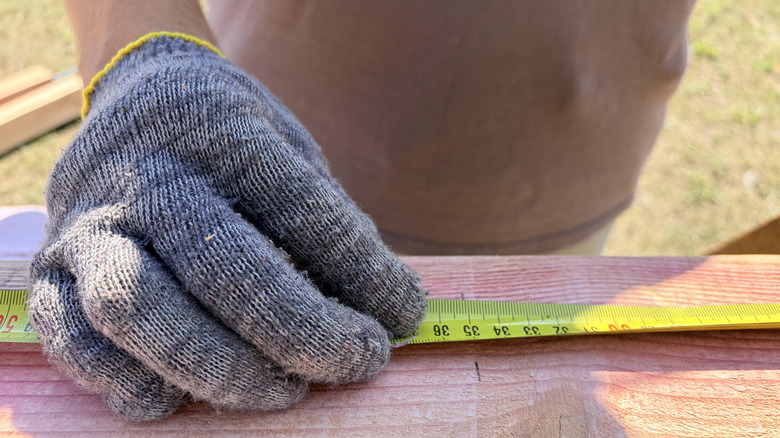 Close-up of a worker measuring a wooden beam with a tape measure outdoors.