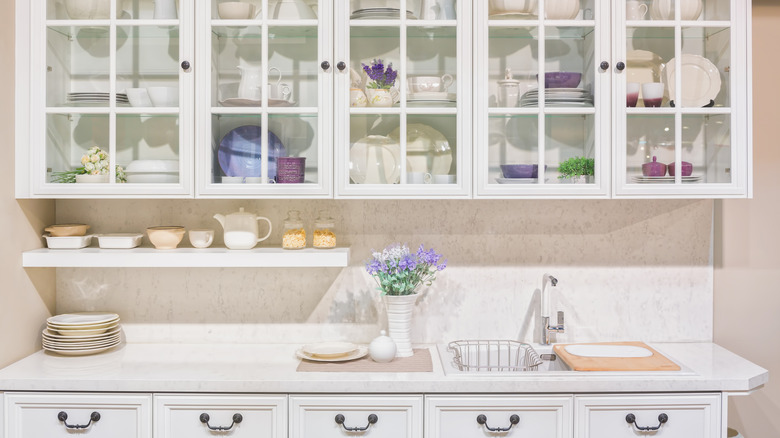 Simple white and glass cabinets with purple and white ceramic plates in chic kitchen