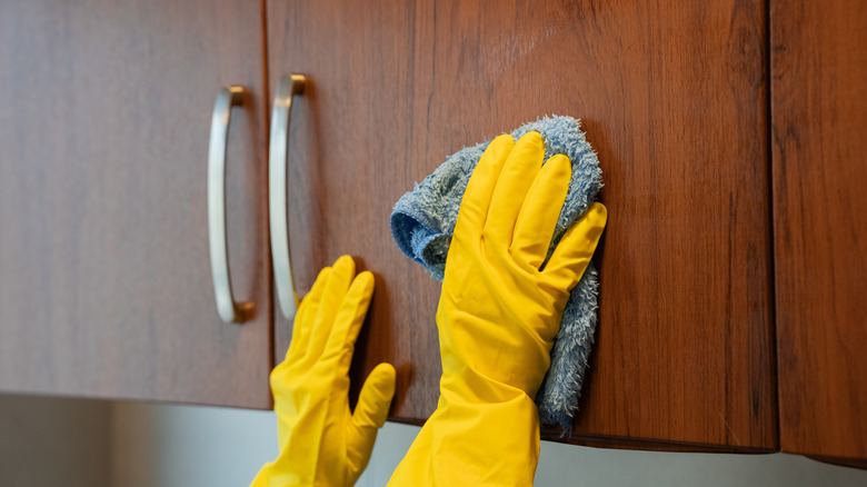 A person wearing gloves uses a cloth to scrub a kitchen cabinet