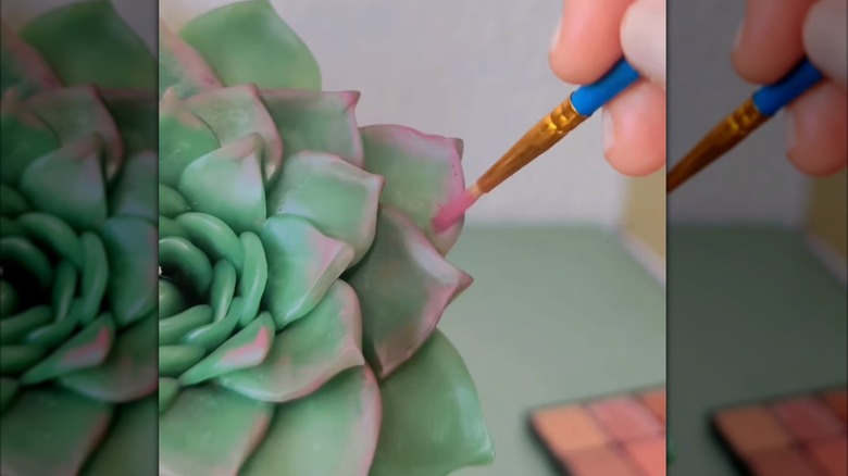 A hand painting pink on the tips of a succulent candle with a small paint brush