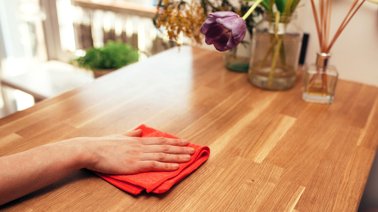 A person uses a red microfiber towel to wipe down a wooden kitchen countertop.