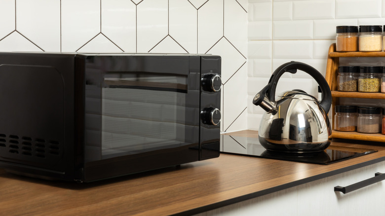 Black microwave on wooden countertop next to a silver kettle