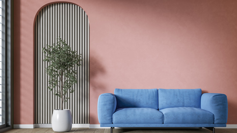 A blue sofa sits in front of neutral pink wall, minimalist plant pot