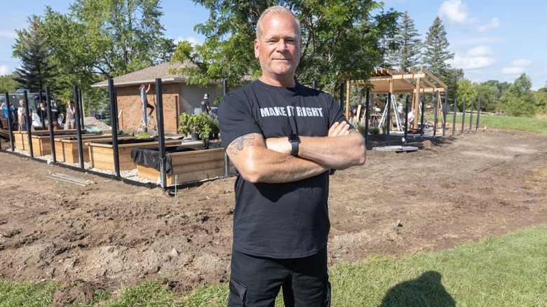 Mike Holmes facing the camera and smiling in front of a raised garden bed outdoor construction project