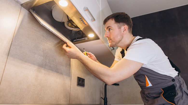 Professional repairing an extractor fan in a modern kitchen