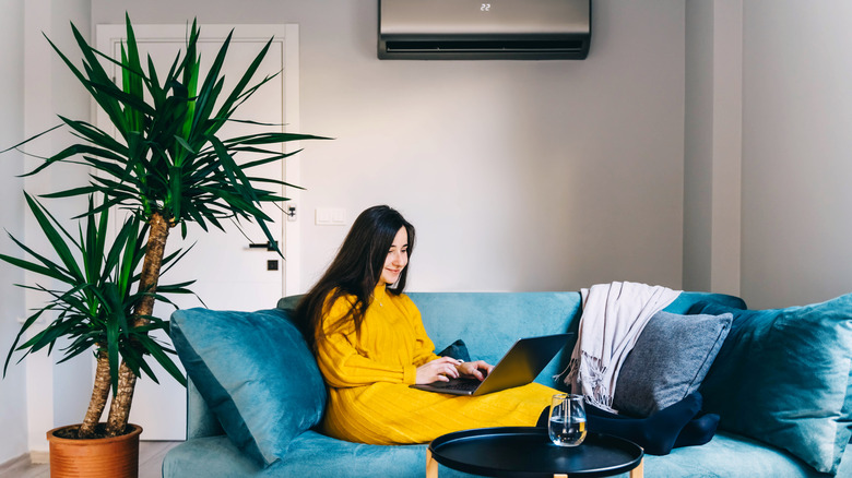 Woman sitting on the couch on her laptop with air conditioner running in the background