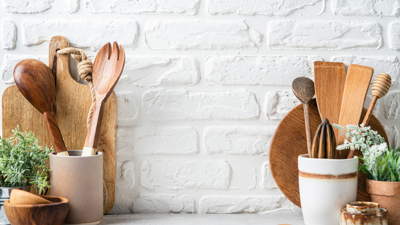 Wooden kitchen utensils and chopping boards displayed against a brick wall painted in white.