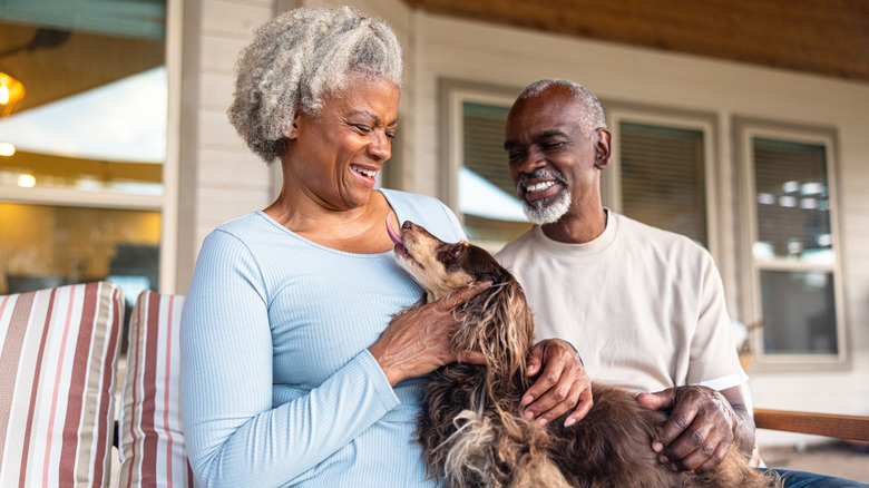 Older couple and small dog sitting on the porch of their home