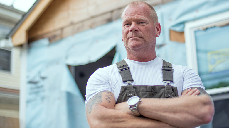 Mike Holmes posing, arms crossed, in front of construction project