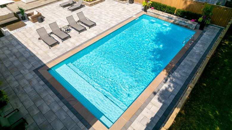 Aerial view of a fenced-in paver patio with in-ground swimming pool