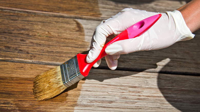 A person applying protective varnish on the deck's wooden flooring