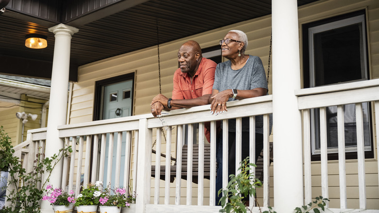 Older couple leaning on the railing of their porch looking out at the neighborhood.