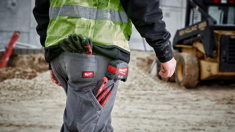 Person carrying tools in Milwaukee-branded work pants
