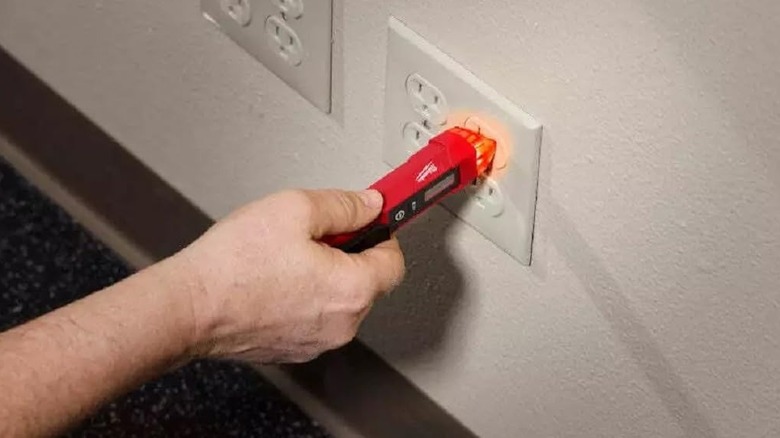 Person using a Milwaukee voltage tester on an outlet