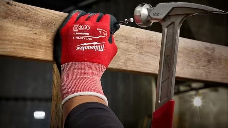 Individual wearing gloves while hammering a nail in a board