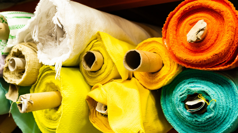 Large rolls of colorful fabric stocked on a shelf.