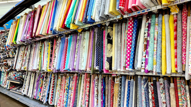 Bolts of various colored fabric on shelves in a Walmart store.