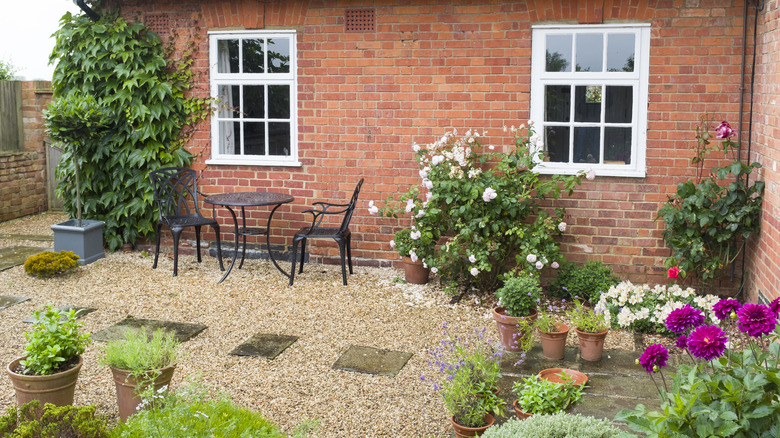 A brick house features a gravel patio surrounded by flowering plants
