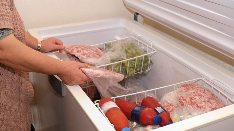 person holding meat in chest freezer