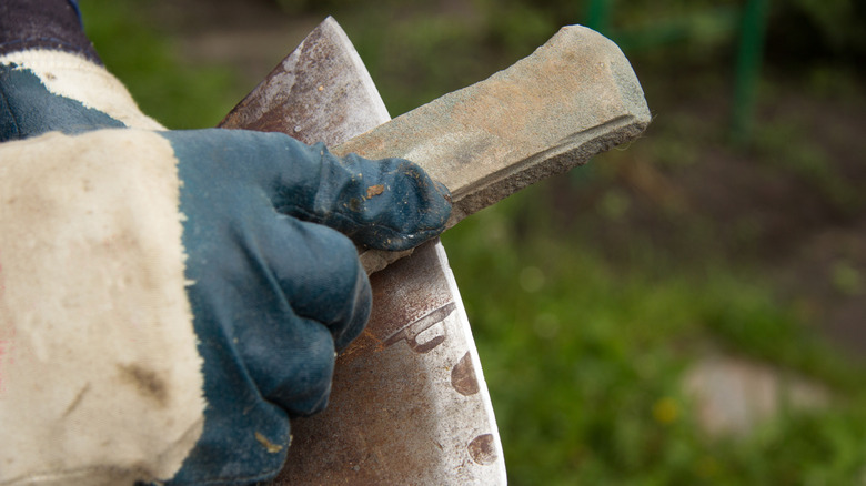 Close-up of gloved hands sharpening an axe with a whetstone