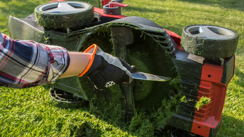 A lawn mower tipped on its side as its owner scrapes grass from the cutting bay