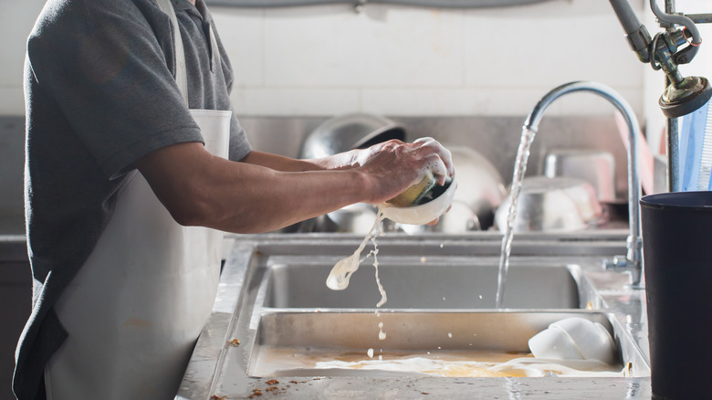 man washing dishes with sponge