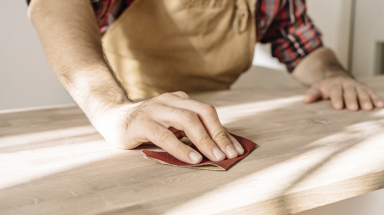 A man sanding a piece of furniture by hand