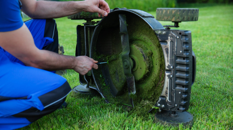 A man wearing overalls fixes a lawnmower blade