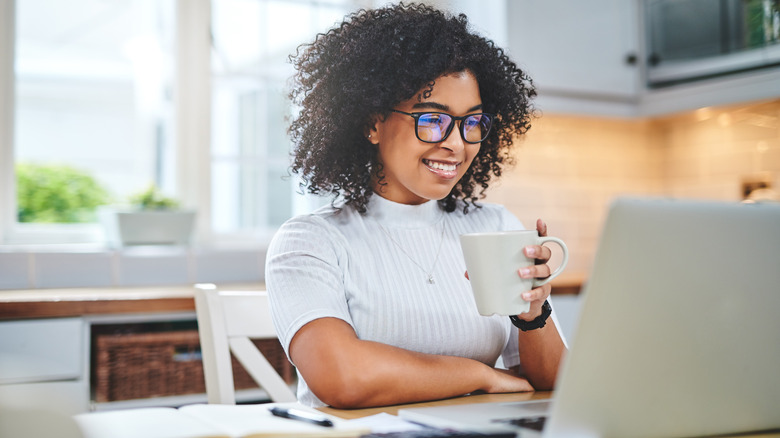 Woman looking at silver laptop with a mug in her hand