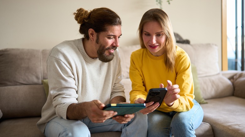 Man and woman comparing prices on a smartphone and tablet