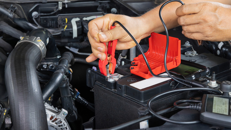 Hand attaching clamp to measure car battery in engine bay