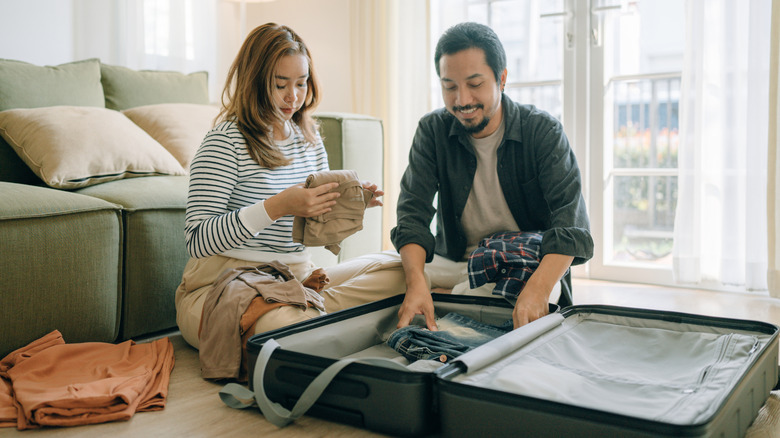 Asian couple packing a suitcase for vacation in their living room