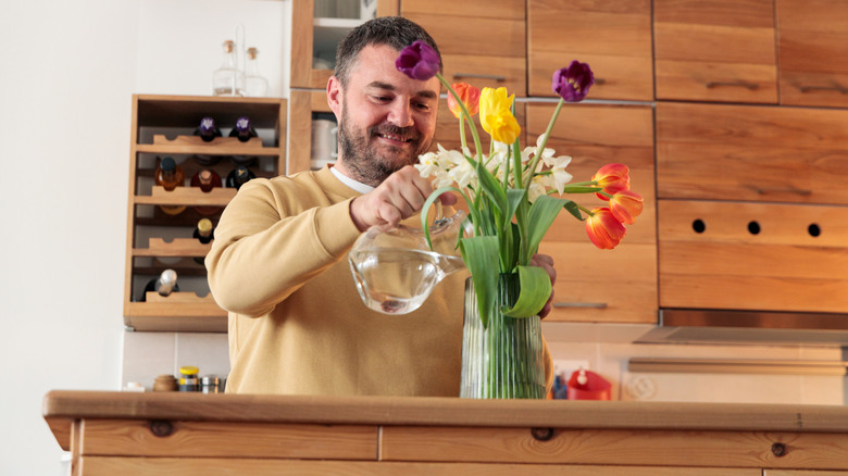 A man adding water to a vase full of flowers
