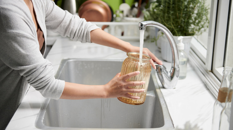 A woman refilling a vase with fresh water at a kitchen sink