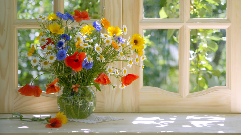 A bouquet of flowers beginning to droop in a sunny windowsill