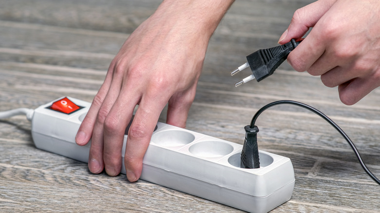 A person plugging a cord into a power strip