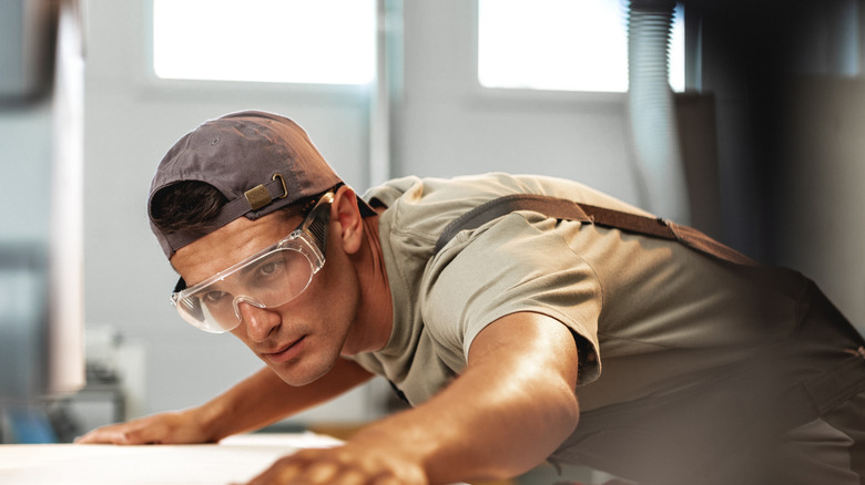 Man in safety glasses examining a piece of wood