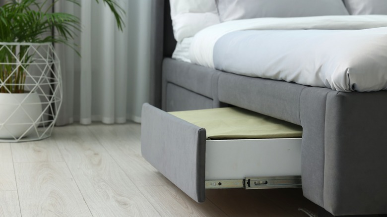 Gray upholstered storage bed with one drawer open holding extra linens