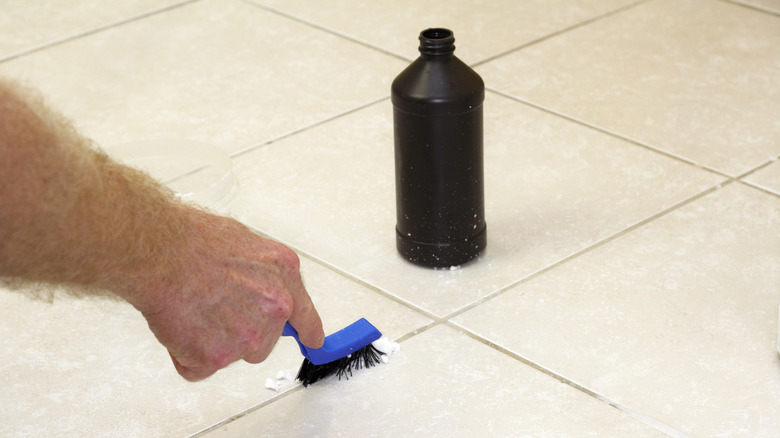 A hand scrubbing tile grout with a bottle of hydrogen peroxide