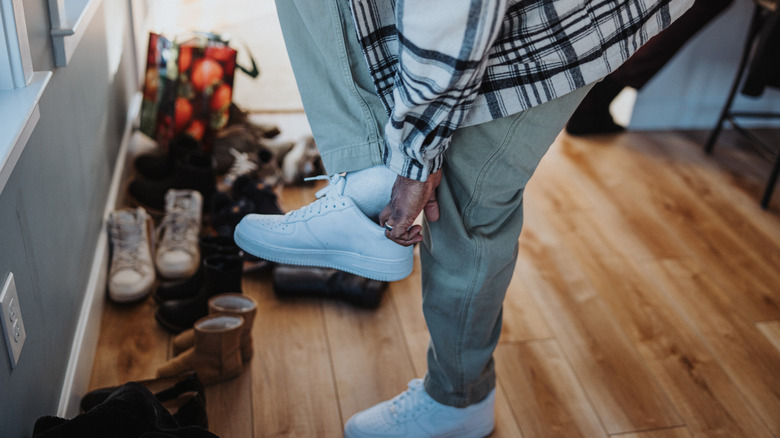 Shoes on the ground by entryway while man puts on white sneakers