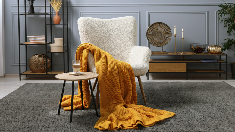 a yellow blanket draped over a fuzzy white accent chair