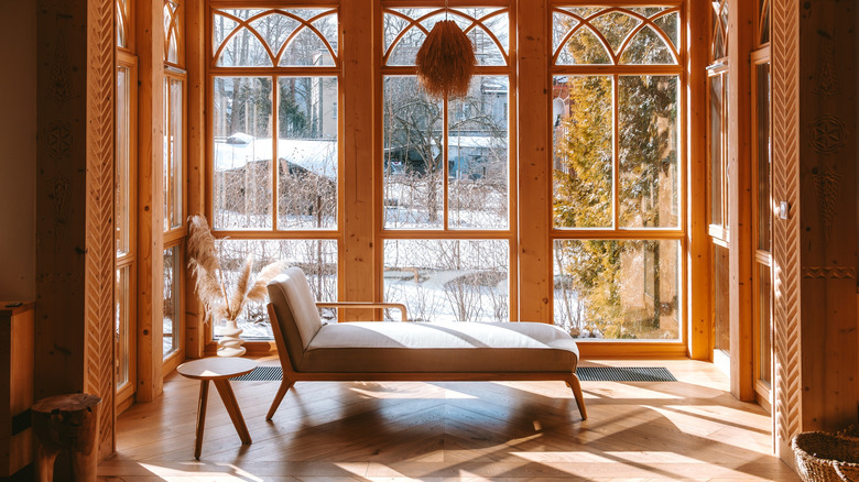 a chaise lounge in front of a window in a sunny wooden room