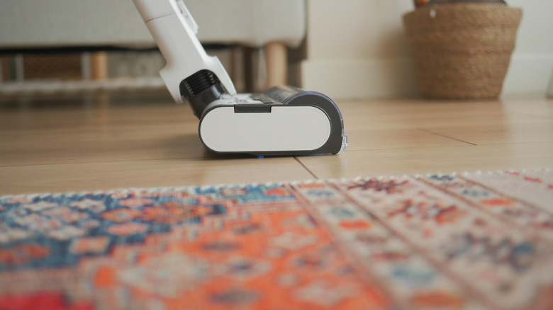 Vacuum cleaner on hardwood floor near colorful rug