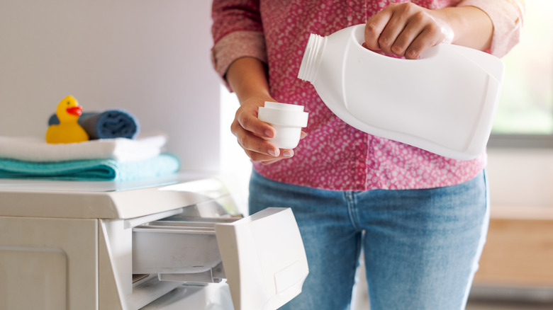 Woman pouring laundry softener in a cap next to washing machine