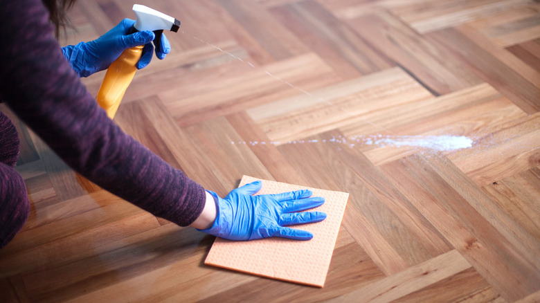 Woman cleaning parquet floor with spray bottle and cloth